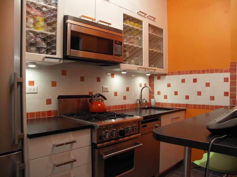 Photo of a small eclectic galley enclosed kitchen in New York with flat-panel cabinets, white cabinets, orange splashback, ceramic splashback, stainless steel appliances and no island.