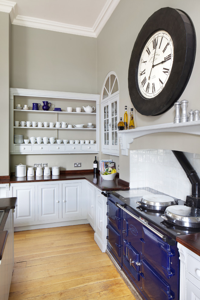 This is an example of a traditional l-shaped kitchen in London with white cabinets, raised-panel cabinets, wood worktops, white splashback, light hardwood flooring and an island.
