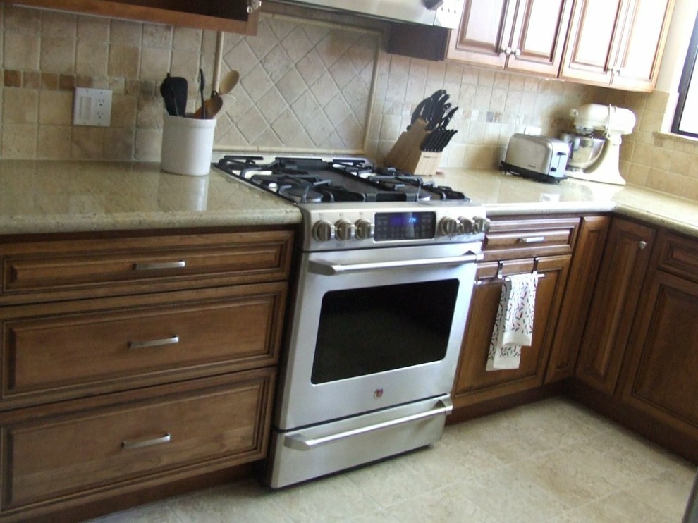 Lantlig inredning av ett avskilt, mellanstort u-kök, med luckor med upphöjd panel, skåp i ljust trä, granitbänkskiva, beige stänkskydd, stänkskydd i stenkakel, svarta vitvaror och en köksö