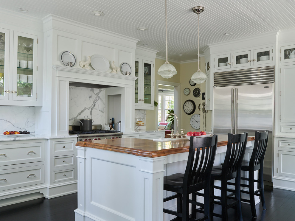 Klassisk inredning av ett kök, med en rustik diskho, marmorbänkskiva, rostfria vitvaror, mörkt trägolv, skåp i shakerstil, vita skåp, vitt stänkskydd och en köksö