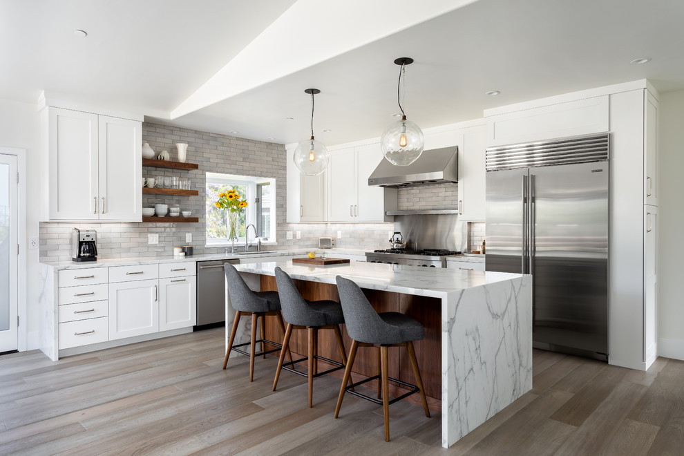 Transitional l-shaped medium tone wood floor and gray floor kitchen photo in San Diego with an undermount sink, shaker cabinets, white cabinets, gray backsplash, stainless steel appliances, an island and white countertops