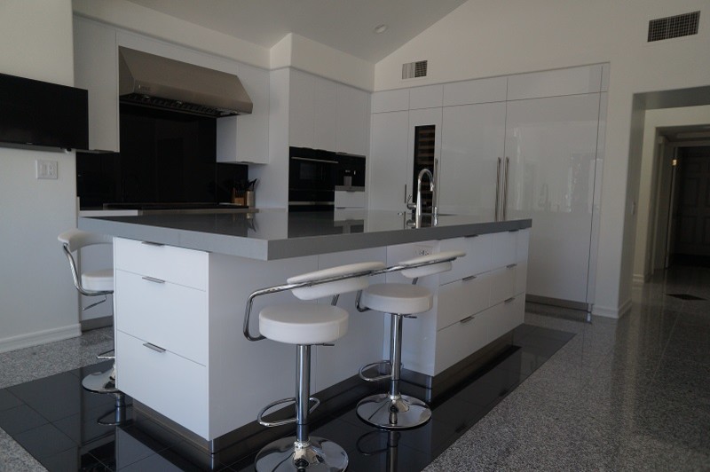 Modern inredning av ett stort kök, med en dubbel diskho, släta luckor, vita skåp, bänkskiva i glas, svart stänkskydd, stänkskydd i glaskakel, rostfria vitvaror, klinkergolv i porslin och en köksö