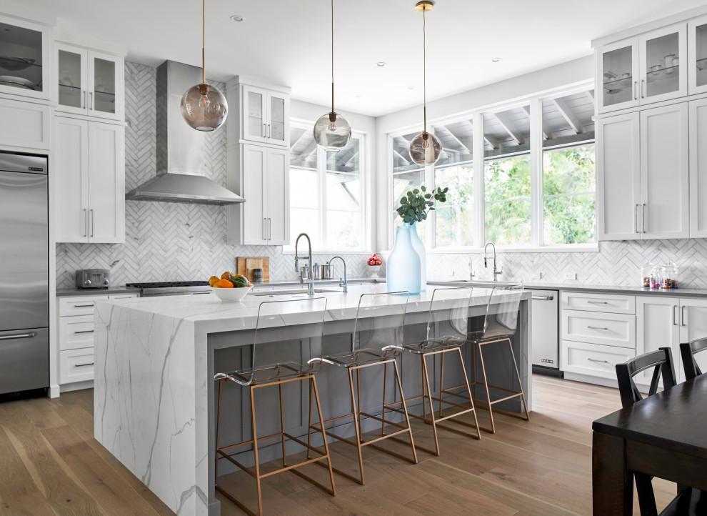 Transitional l-shaped medium tone wood floor and brown floor eat-in kitchen photo in Austin with shaker cabinets, white cabinets, white backsplash, stainless steel appliances, an island and gray countertops
