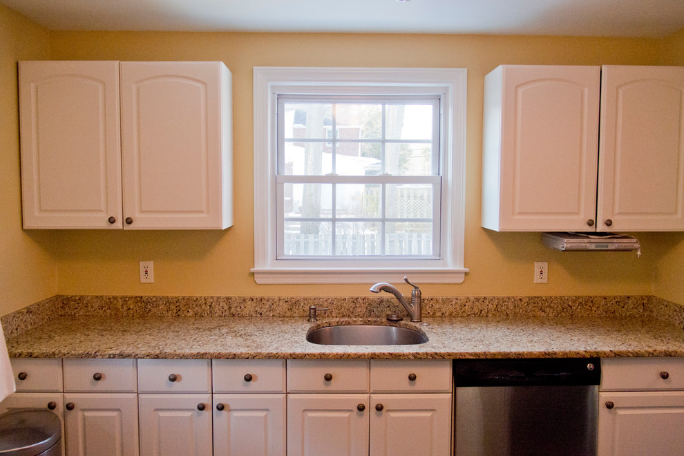 Cette image montre une petite cuisine linéaire traditionnelle fermée avec un placard avec porte à panneau encastré, des portes de placard blanches, un plan de travail en granite et un évier encastré.