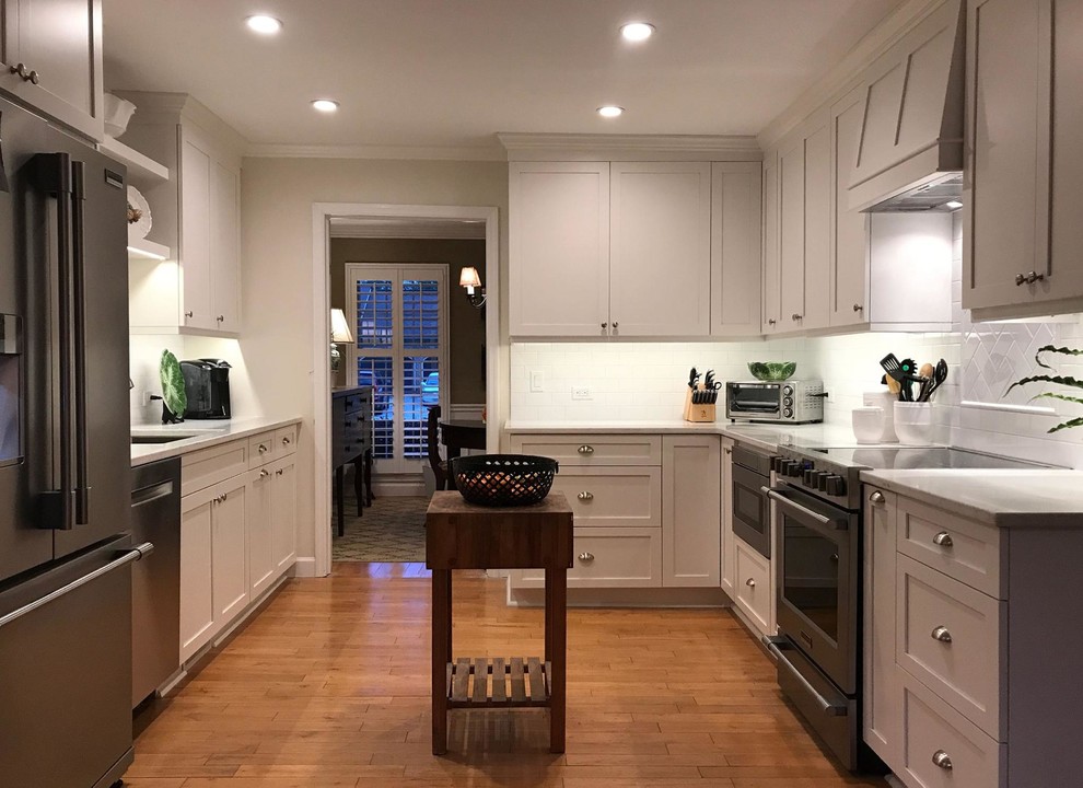 Mid-sized elegant u-shaped medium tone wood floor and brown floor enclosed kitchen photo in Charleston with an undermount sink, shaker cabinets, white cabinets, solid surface countertops, white backsplash, subway tile backsplash, stainless steel appliances and no island