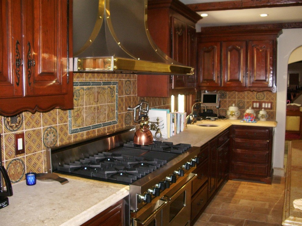 Inredning av ett medelhavsstil mellanstort kök, med luckor med upphöjd panel, skåp i mellenmörkt trä, bänkskiva i kalksten, stänkskydd i keramik, rostfria vitvaror, tegelgolv och en köksö