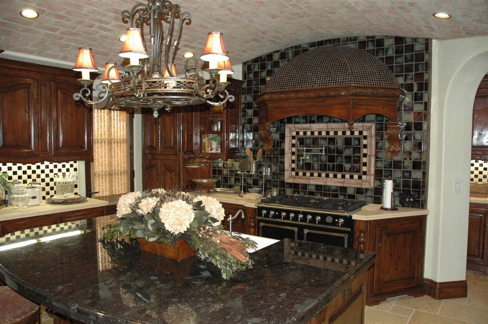 Idéer för att renovera ett mellanstort medelhavsstil linjärt kök och matrum, med en rustik diskho, luckor med upphöjd panel, skåp i mörkt trä, kaklad bänkskiva, flerfärgad stänkskydd, stänkskydd i mosaik, svarta vitvaror, travertin golv och en köksö