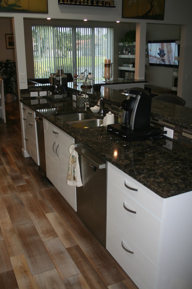 Example of a minimalist l-shaped eat-in kitchen design in Miami with flat-panel cabinets, white cabinets, granite countertops, beige backsplash, glass tile backsplash, stainless steel appliances and an island