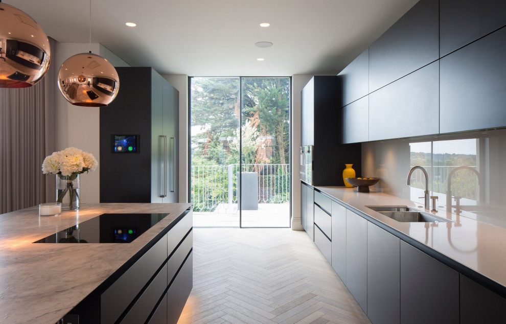 Inredning av ett modernt grå grått kök, med en undermonterad diskho, släta luckor, svarta skåp, grått stänkskydd, glaspanel som stänkskydd, mellanmörkt trägolv, en köksö och brunt golv