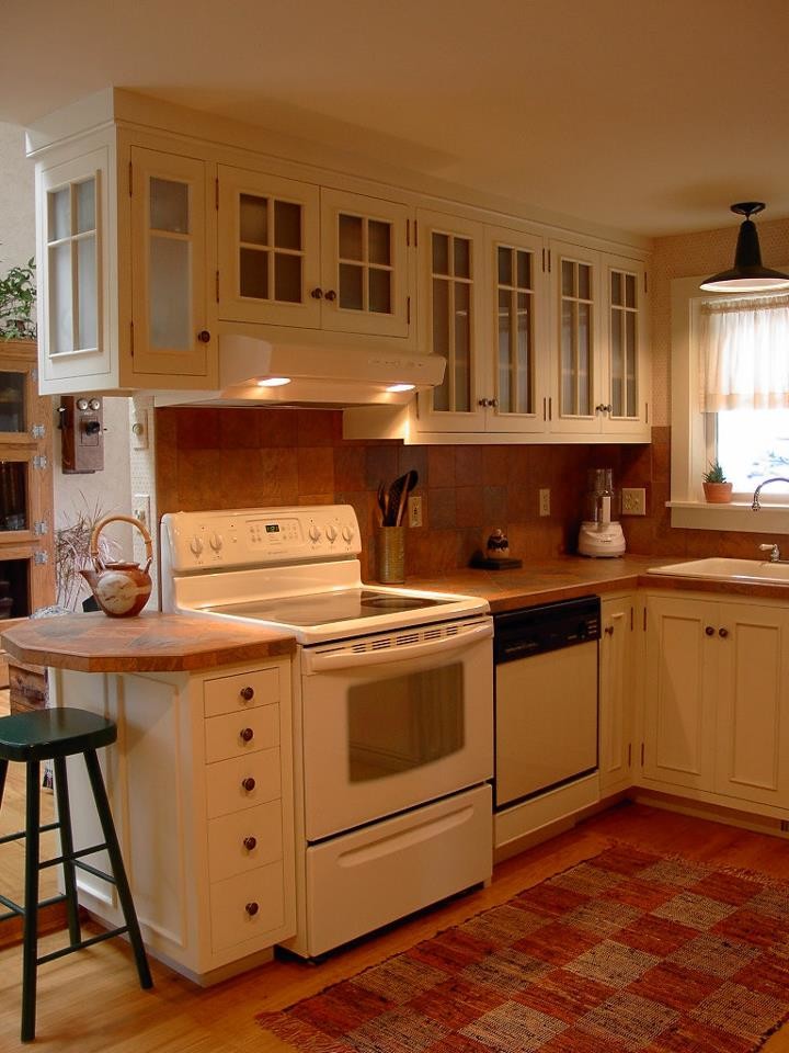 Photo of a small classic l-shaped kitchen/diner in Boston with a single-bowl sink, recessed-panel cabinets, white cabinets, tile countertops, ceramic splashback, white appliances and light hardwood flooring.