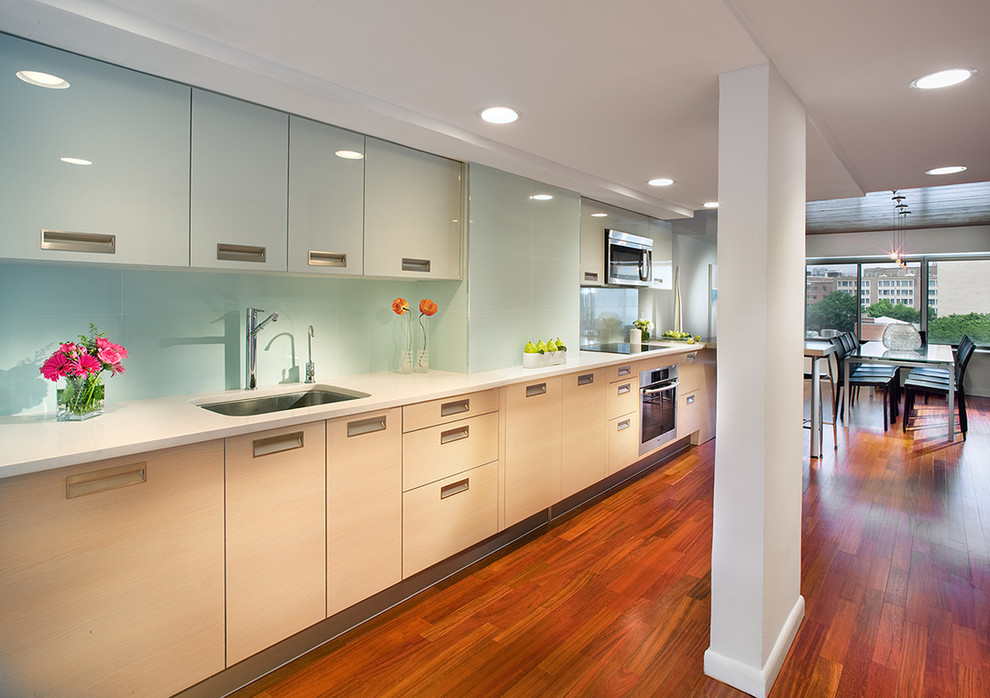 This is an example of a large contemporary single-wall kitchen/diner in New York with flat-panel cabinets, a single-bowl sink, stainless steel appliances, blue splashback, light wood cabinets, glass tiled splashback, medium hardwood flooring, no island and brown floors.