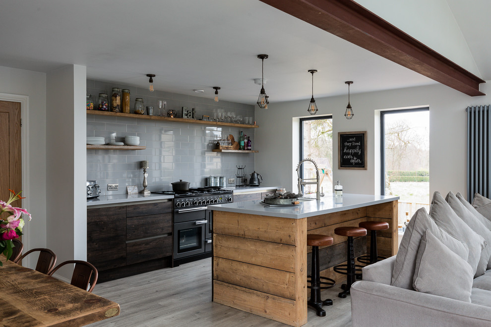 Farmhouse galley kitchen in Cheshire with flat-panel cabinets, dark wood cabinets, grey splashback, black appliances, an island, grey floors and grey worktops.