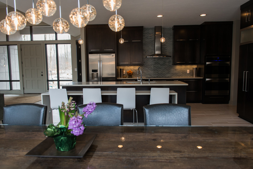 Photo of an expansive modern l-shaped kitchen/diner in Cleveland with a submerged sink, flat-panel cabinets, dark wood cabinets, engineered stone countertops, grey splashback, glass tiled splashback, stainless steel appliances, ceramic flooring and an island.
