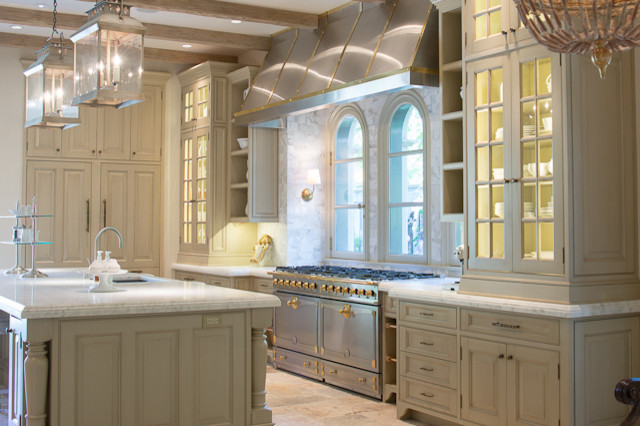 Klassisk inredning av ett stort kök, med en undermonterad diskho, luckor med infälld panel, skåp i slitet trä, marmorbänkskiva, beige stänkskydd, stänkskydd i stenkakel, rostfria vitvaror, kalkstensgolv och en köksö
