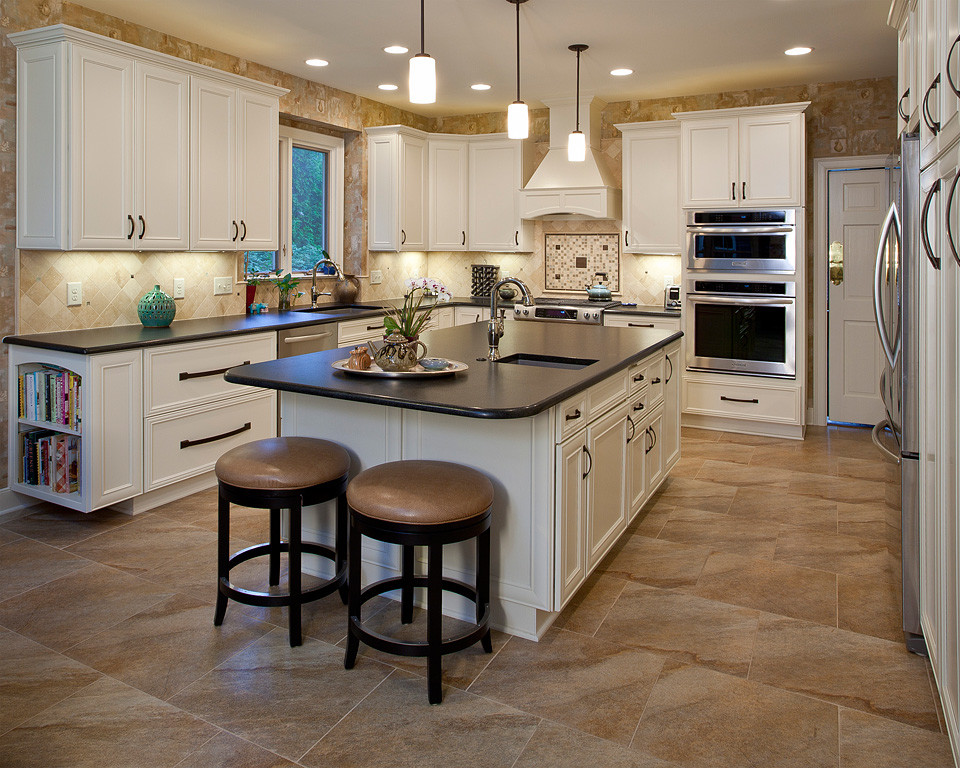 This is an example of a large classic u-shaped kitchen/diner in Raleigh with an island, a submerged sink, beige splashback, porcelain splashback, stainless steel appliances, porcelain flooring, beaded cabinets, white cabinets, composite countertops, brown floors and black worktops.