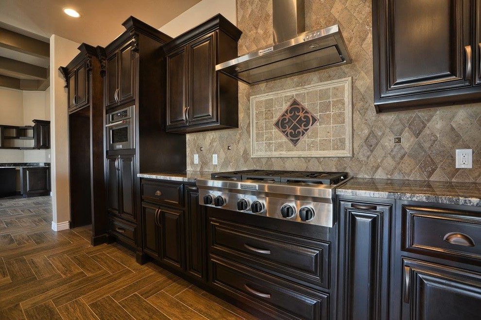 This is an example of a large classic l-shaped open plan kitchen in Austin with a submerged sink, raised-panel cabinets, dark wood cabinets, granite worktops, beige splashback, cement tile splashback, stainless steel appliances, medium hardwood flooring, an island and brown floors.