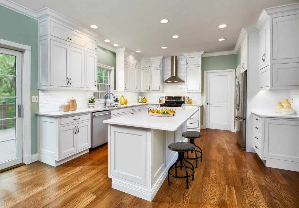 Inspiration for a mid-sized timeless u-shaped medium tone wood floor and brown floor kitchen remodel in Indianapolis with an undermount sink, white cabinets, white backsplash, subway tile backsplash, stainless steel appliances, an island, white countertops and beaded inset cabinets