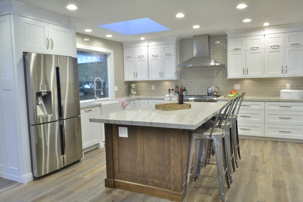 Modern inredning av ett mellanstort kök, med en rustik diskho, skåp i shakerstil, vita skåp, bänkskiva i kvartsit, grått stänkskydd, stänkskydd i tunnelbanekakel, rostfria vitvaror, mellanmörkt trägolv och en köksö