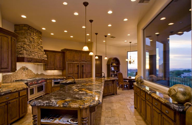Medelhavsstil inredning av ett stort kök, med luckor med upphöjd panel, skåp i mellenmörkt trä, granitbänkskiva, beige stänkskydd, stänkskydd i stenkakel, rostfria vitvaror, travertin golv och en köksö