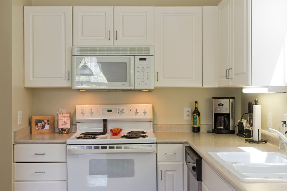 This is an example of a small classic l-shaped enclosed kitchen in Raleigh with a double-bowl sink, raised-panel cabinets, white cabinets, laminate countertops, white appliances, ceramic flooring and no island.