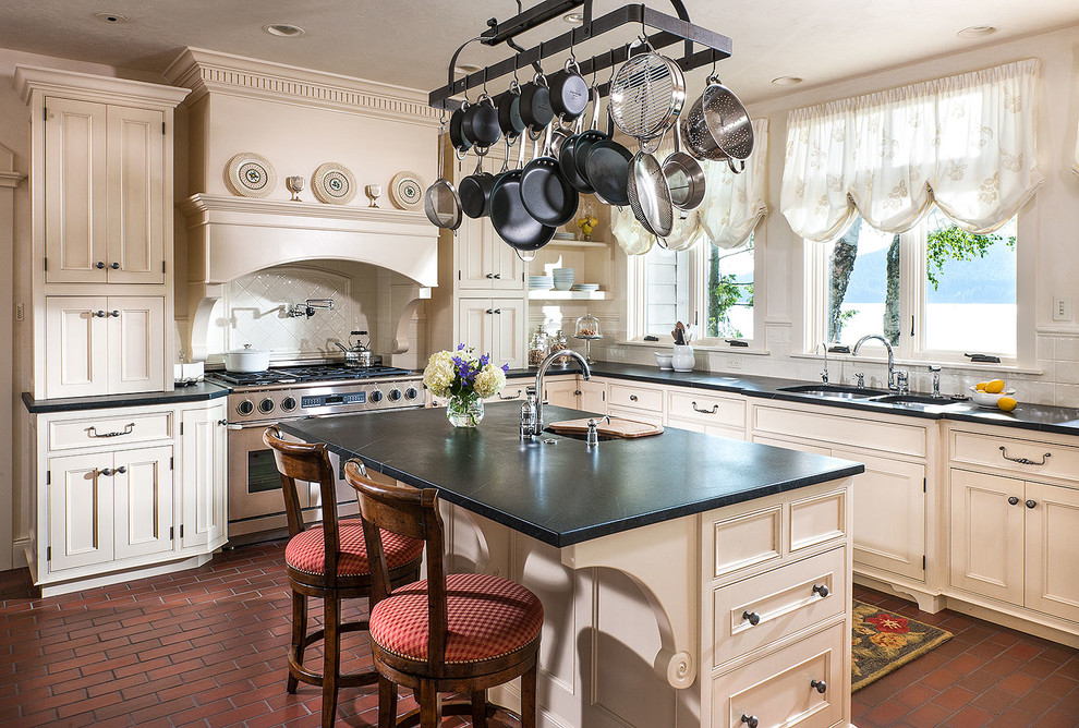Mid-sized country l-shaped brick floor eat-in kitchen photo in Other with a double-bowl sink, recessed-panel cabinets, white cabinets, soapstone countertops, white backsplash, ceramic backsplash, stainless steel appliances and an island