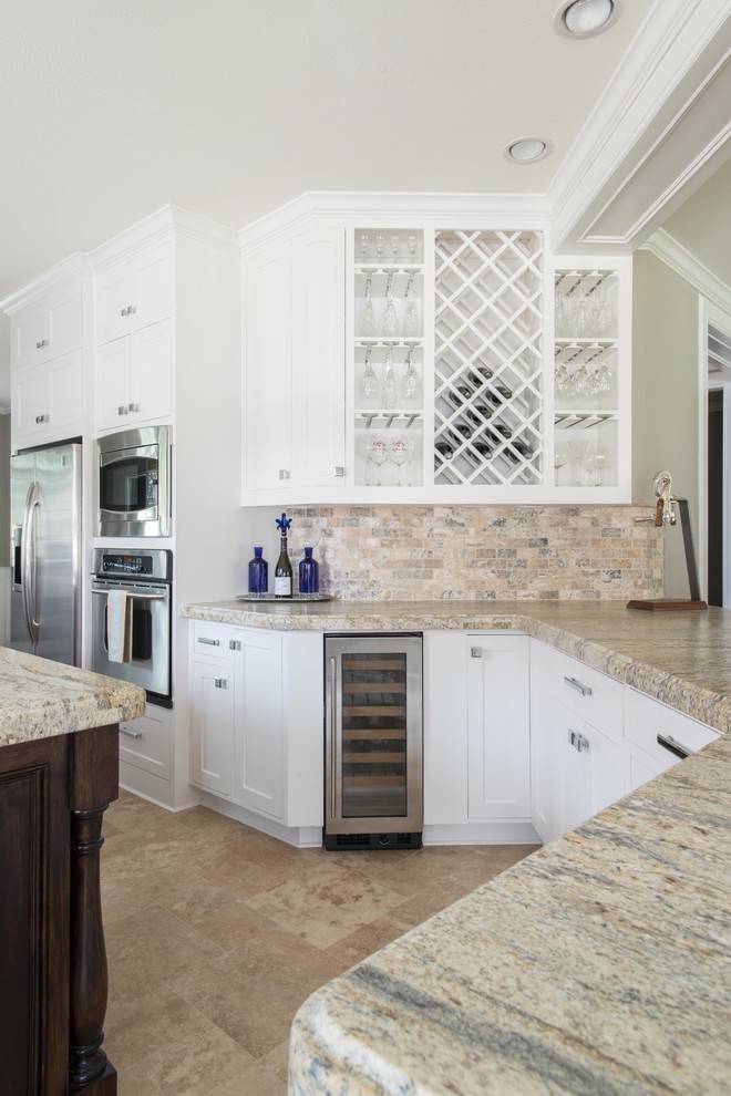 Inspiration for a mid-sized transitional galley travertine floor eat-in kitchen remodel in Houston with an undermount sink, recessed-panel cabinets, white cabinets, granite countertops, brown backsplash, stone tile backsplash, stainless steel appliances and an island