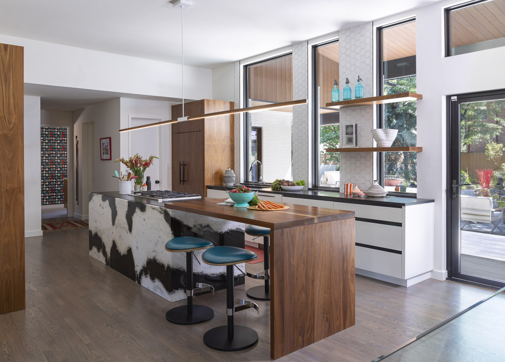 Inspiration for a medium sized contemporary galley kitchen/diner in Denver with flat-panel cabinets, white cabinets, wood worktops, dark hardwood flooring, an island, a submerged sink, white splashback, window splashback, integrated appliances, brown floors and black worktops.