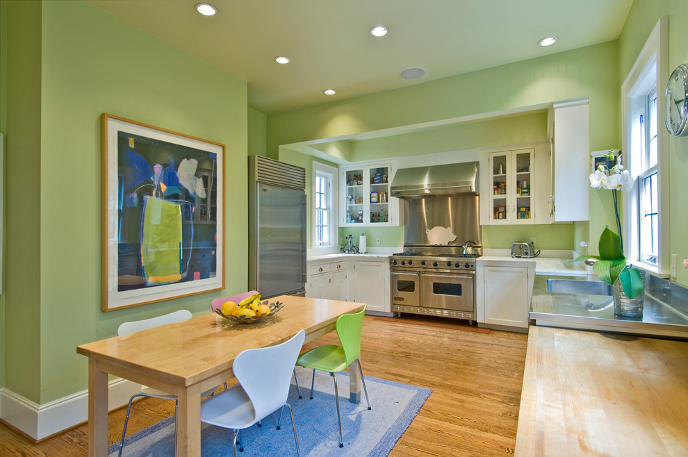 Cette photo montre une cuisine américaine tendance en U avec un placard avec porte à panneau encastré, des portes de placard blanches, un plan de travail en inox et un électroménager en acier inoxydable.