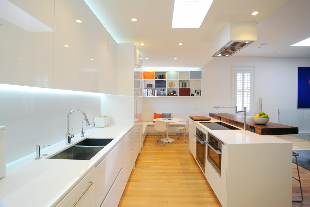 На фото: параллельная кухня в стиле модернизм с обеденным столом, двойной мойкой, плоскими фасадами, белыми фасадами, деревянной столешницей и техникой из нержавеющей стали