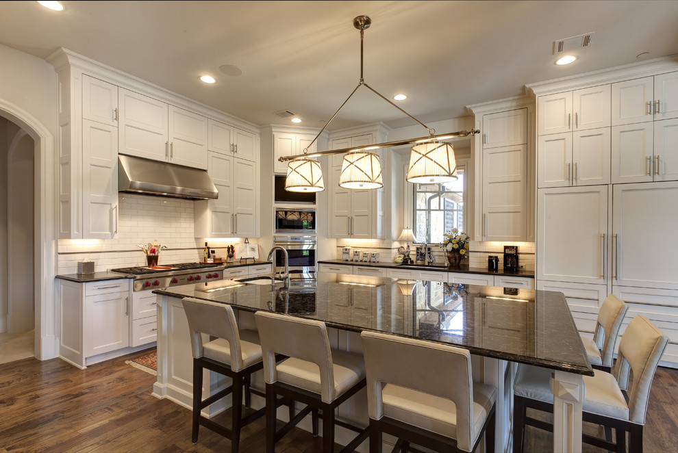 Klassische Küche mit Waschbecken, Küchenrückwand in Weiß, Küchengeräten aus Edelstahl, braunem Holzboden und Kücheninsel in Dallas