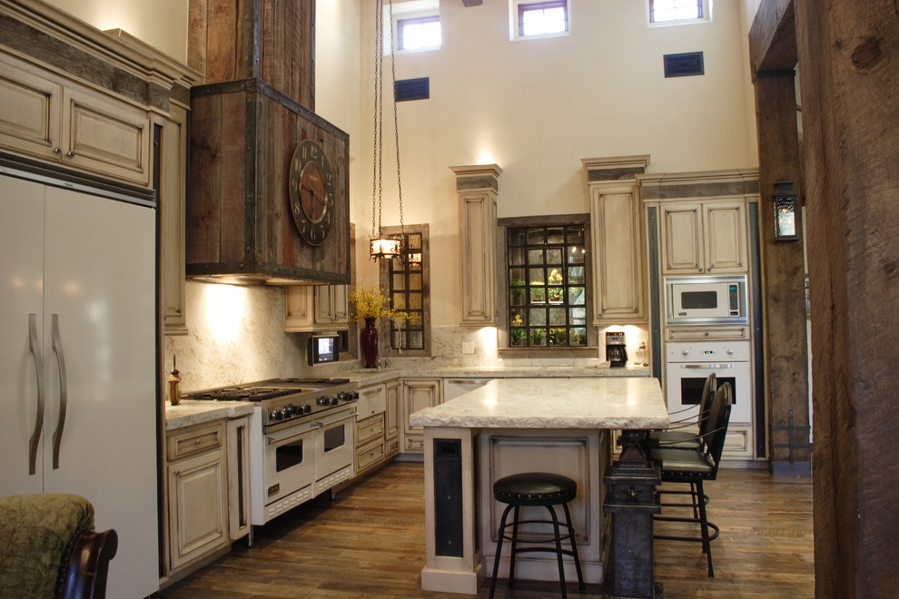 Example of a large southwest l-shaped medium tone wood floor eat-in kitchen design in Phoenix with raised-panel cabinets, distressed cabinets, solid surface countertops, beige backsplash, stone slab backsplash, white appliances and an island