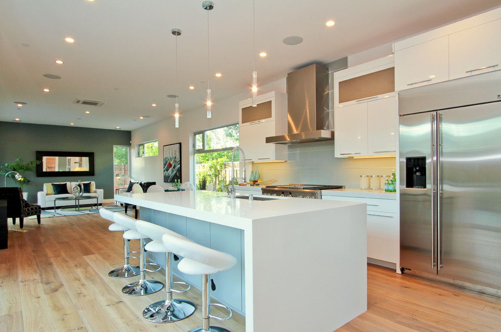 Example of a trendy single-wall light wood floor open concept kitchen design in San Francisco with an undermount sink, flat-panel cabinets, white cabinets, solid surface countertops, blue backsplash, ceramic backsplash, stainless steel appliances and an island