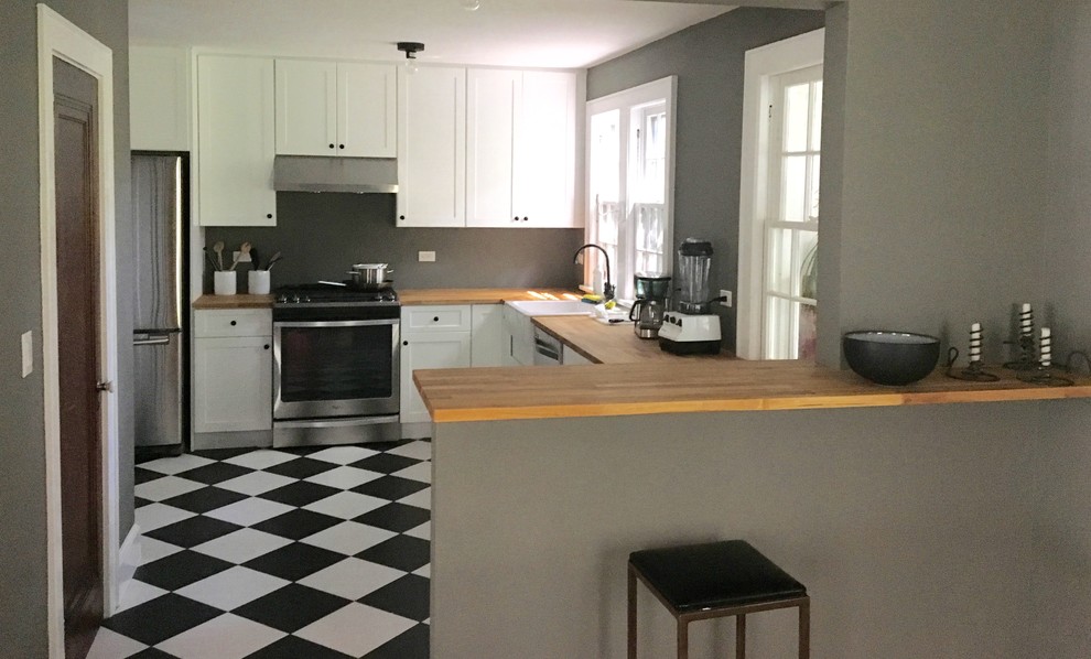 This is an example of a classic l-shaped kitchen/diner in New York with a belfast sink, raised-panel cabinets, beige cabinets, granite worktops, black splashback, cement tile splashback, stainless steel appliances, an island and lino flooring.