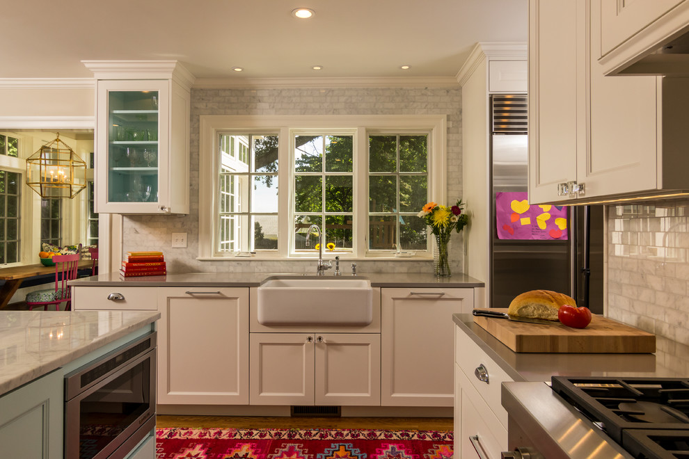 Photo of a medium sized classic kitchen in Boston with a belfast sink, recessed-panel cabinets, white cabinets, grey splashback, ceramic splashback, stainless steel appliances, medium hardwood flooring and an island.