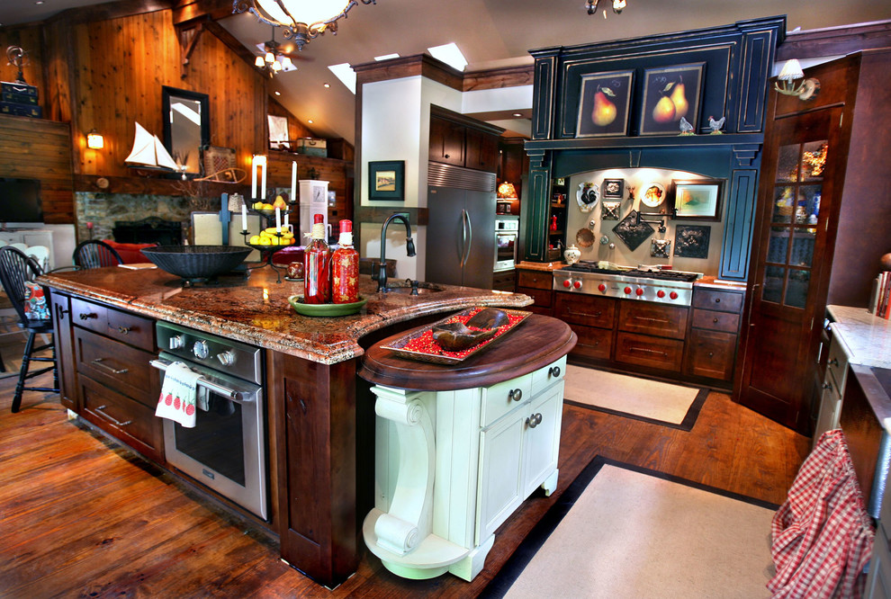 Inspiration for a large rustic l-shaped kitchen/diner in Indianapolis with a belfast sink, recessed-panel cabinets, dark wood cabinets, granite worktops, stainless steel appliances, dark hardwood flooring, an island, brown floors and red worktops.