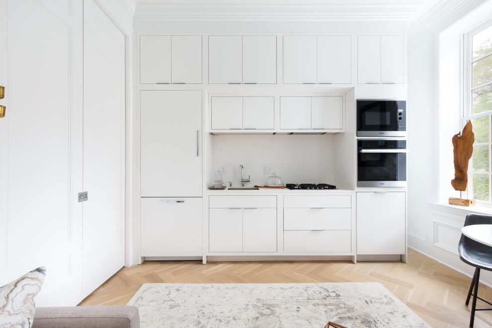 Scandinavian single-wall kitchen/diner in Other with flat-panel cabinets, white cabinets, white splashback, stainless steel appliances, light hardwood flooring, no island and beige floors.