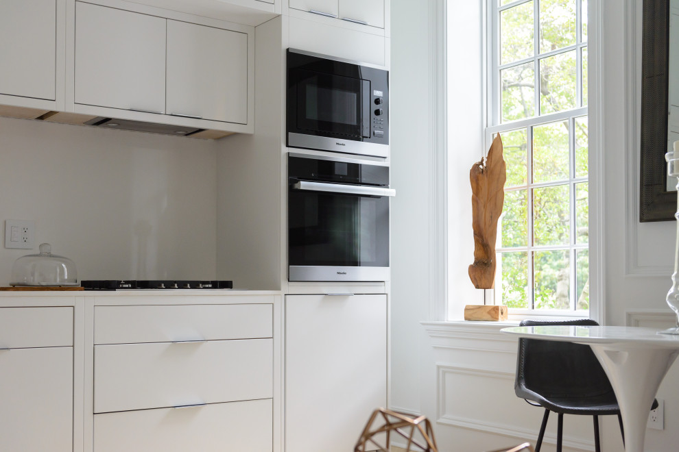 Exempel på ett minimalistiskt linjärt kök och matrum, med släta luckor, vita skåp, vitt stänkskydd, rostfria vitvaror, ljust trägolv och beiget golv
