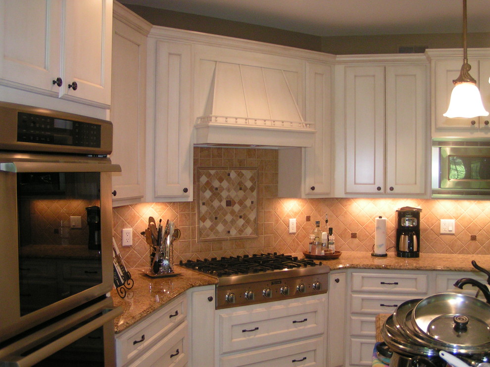 Klassisk inredning av ett kök och matrum, med luckor med infälld panel, vita skåp, granitbänkskiva, beige stänkskydd, stänkskydd i porslinskakel och rostfria vitvaror