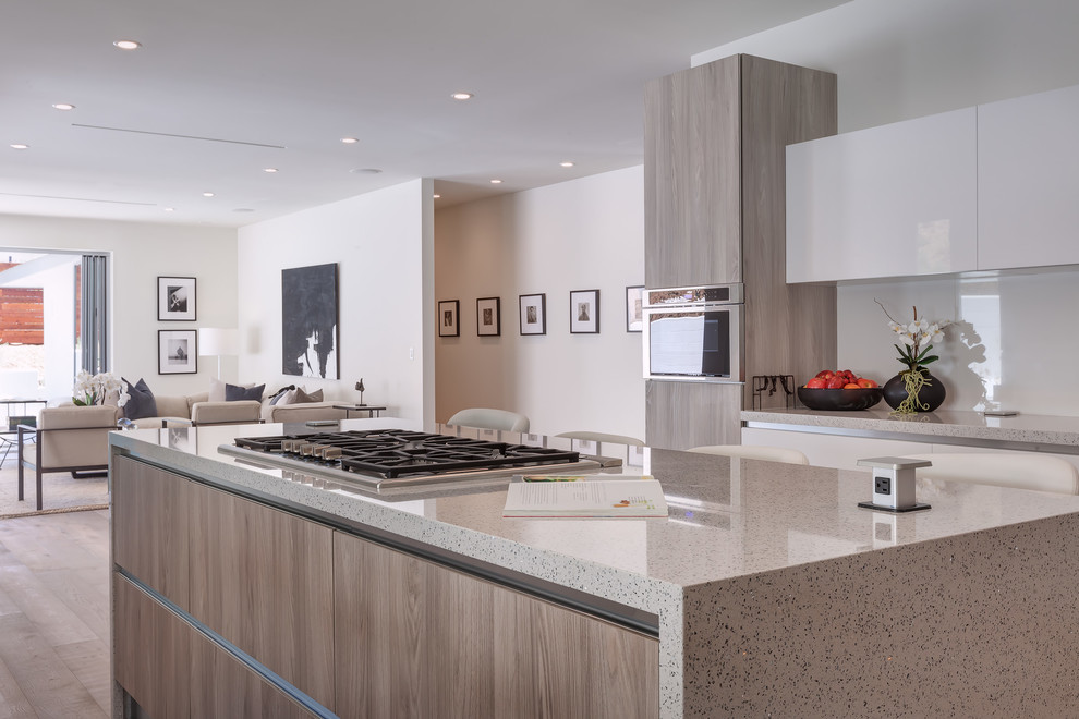 Large contemporary u-shaped open plan kitchen in Los Angeles with flat-panel cabinets, light wood cabinets, engineered stone countertops, white splashback, glass sheet splashback, stainless steel appliances, porcelain flooring, an island and grey worktops.