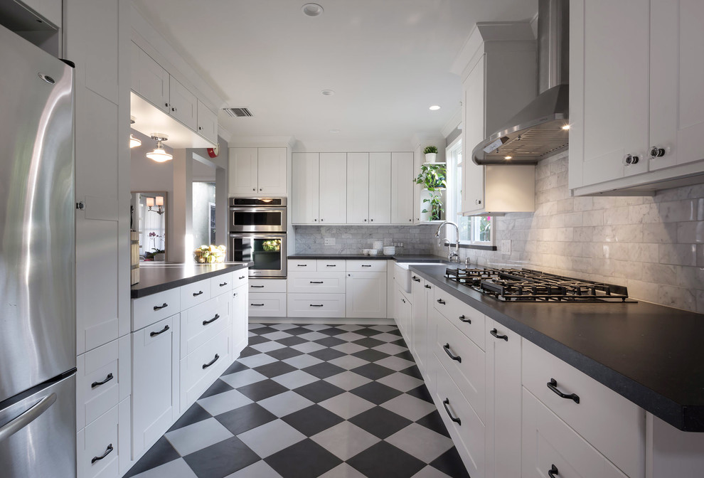 Medium sized eclectic galley kitchen/diner with a belfast sink, shaker cabinets, white cabinets, engineered stone countertops, white splashback, marble splashback, stainless steel appliances, porcelain flooring, multi-coloured floors and black worktops.