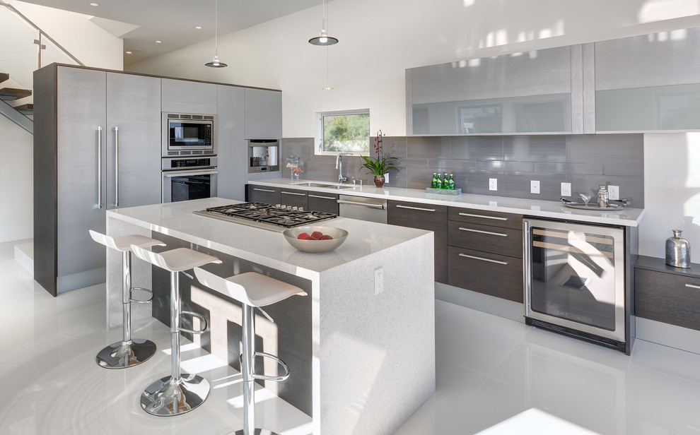 Inspiration for a large contemporary l-shaped open plan kitchen in Los Angeles with a submerged sink, flat-panel cabinets, dark wood cabinets, grey splashback, stainless steel appliances, an island, engineered stone countertops, porcelain splashback, porcelain flooring, white floors and grey worktops.