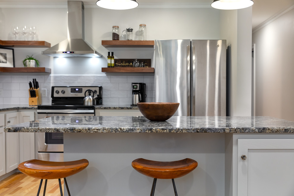 Exempel på ett mellanstort lantligt grå grått kök, med en undermonterad diskho, skåp i shakerstil, grå skåp, granitbänkskiva, vitt stänkskydd, stänkskydd i tunnelbanekakel, rostfria vitvaror, ljust trägolv, en köksö och beiget golv