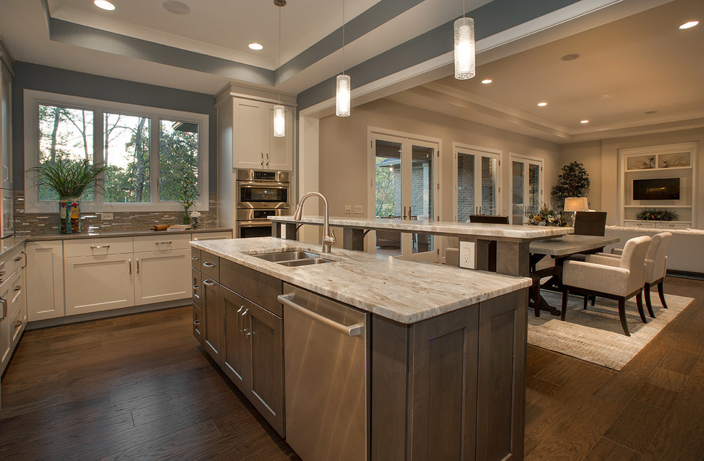 Large modern u-shaped open plan kitchen in Cincinnati with a built-in sink, flat-panel cabinets, grey cabinets, granite worktops, beige splashback, glass tiled splashback, stainless steel appliances, medium hardwood flooring and an island.