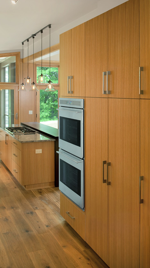 Moderne Küche mit flächenbündigen Schrankfronten, Küchengeräten aus Edelstahl, braunem Holzboden und Kücheninsel in Grand Rapids