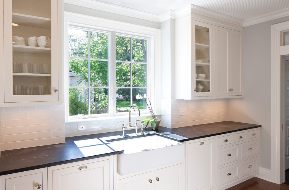 Inspiration for a medium sized classic galley kitchen/diner in Grand Rapids with a belfast sink, white cabinets, soapstone worktops, white splashback, metro tiled splashback, shaker cabinets, integrated appliances, dark hardwood flooring, an island, brown floors and black worktops.
