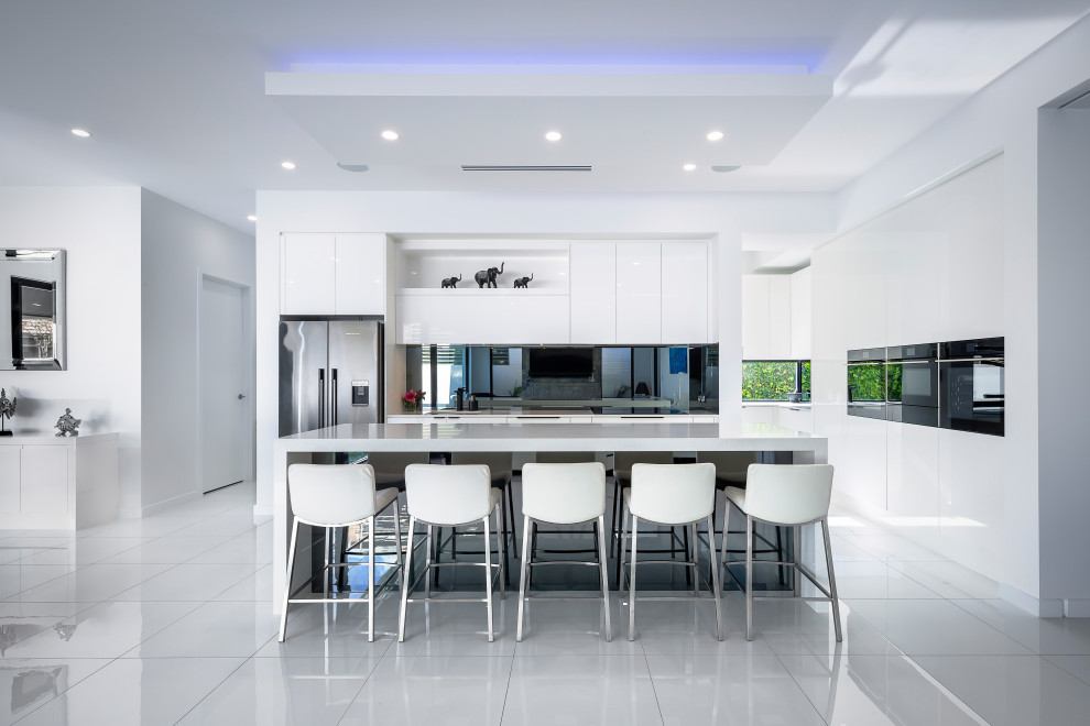 Moderne Küche in L-Form mit flächenbündigen Schrankfronten, weißen Schränken, Küchengeräten aus Edelstahl, Kücheninsel, grauem Boden und weißer Arbeitsplatte in Adelaide