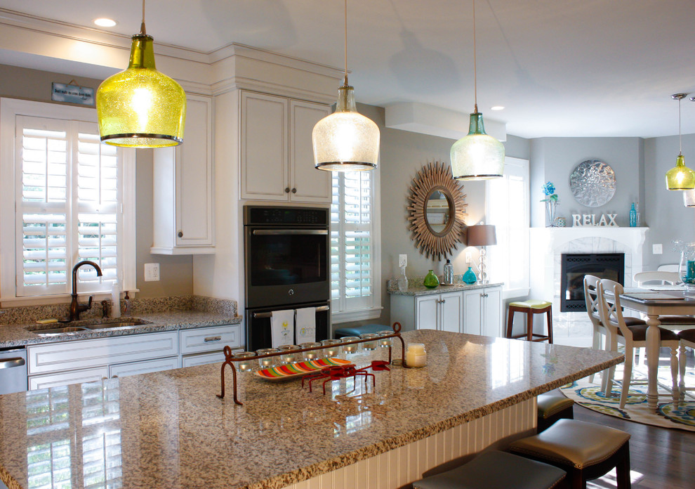 Klassisk inredning av ett mellanstort kök, med vita skåp, granitbänkskiva, flerfärgad stänkskydd, stänkskydd i stickkakel, rostfria vitvaror, mellanmörkt trägolv och en köksö