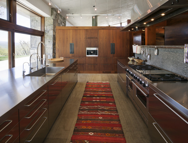 Example of a large urban single-wall eat-in kitchen design in Denver with an undermount sink, flat-panel cabinets, dark wood cabinets, stainless steel countertops, blue backsplash, glass sheet backsplash, stainless steel appliances and an island