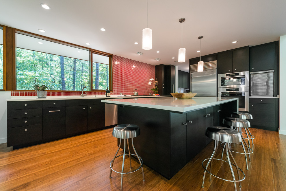 L-shaped eat-in kitchen photo in Atlanta with a drop-in sink, flat-panel cabinets, black cabinets, red backsplash and stainless steel appliances
