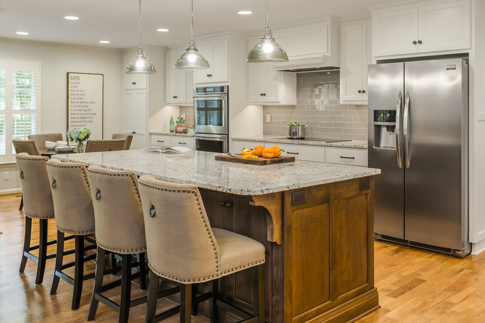 Inspiration for a mid-sized medium tone wood floor and brown floor eat-in kitchen remodel in Atlanta with an undermount sink, recessed-panel cabinets, white cabinets, granite countertops, gray backsplash, ceramic backsplash, stainless steel appliances and an island